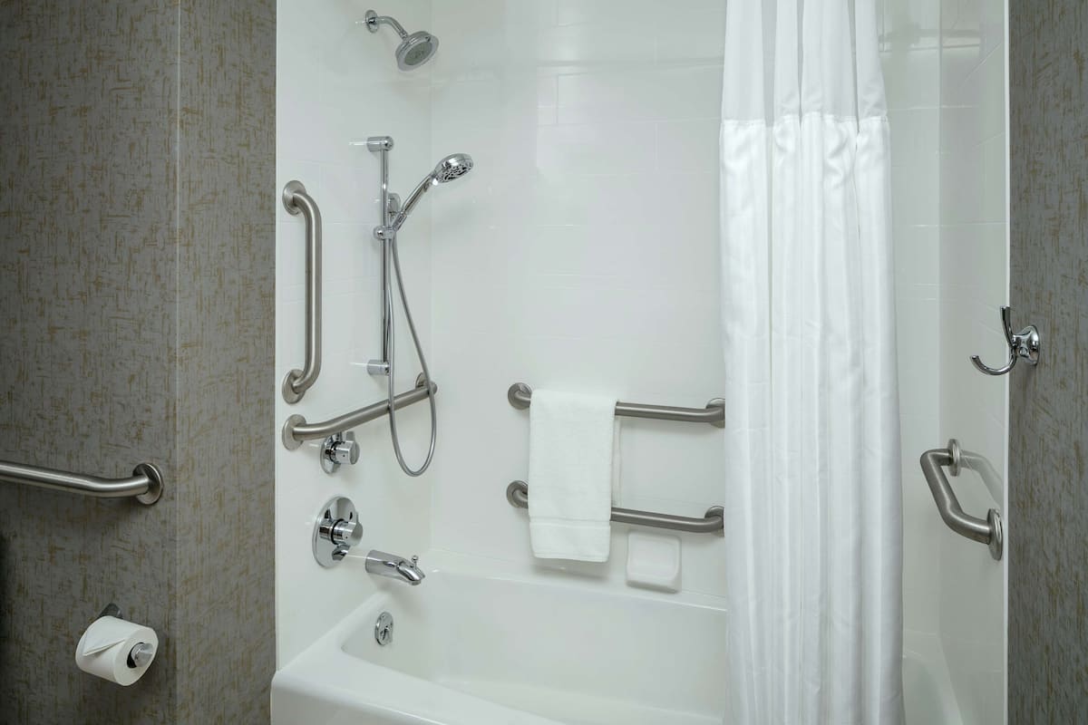 A bathroom with a bathtub, shower, and grab bars.
