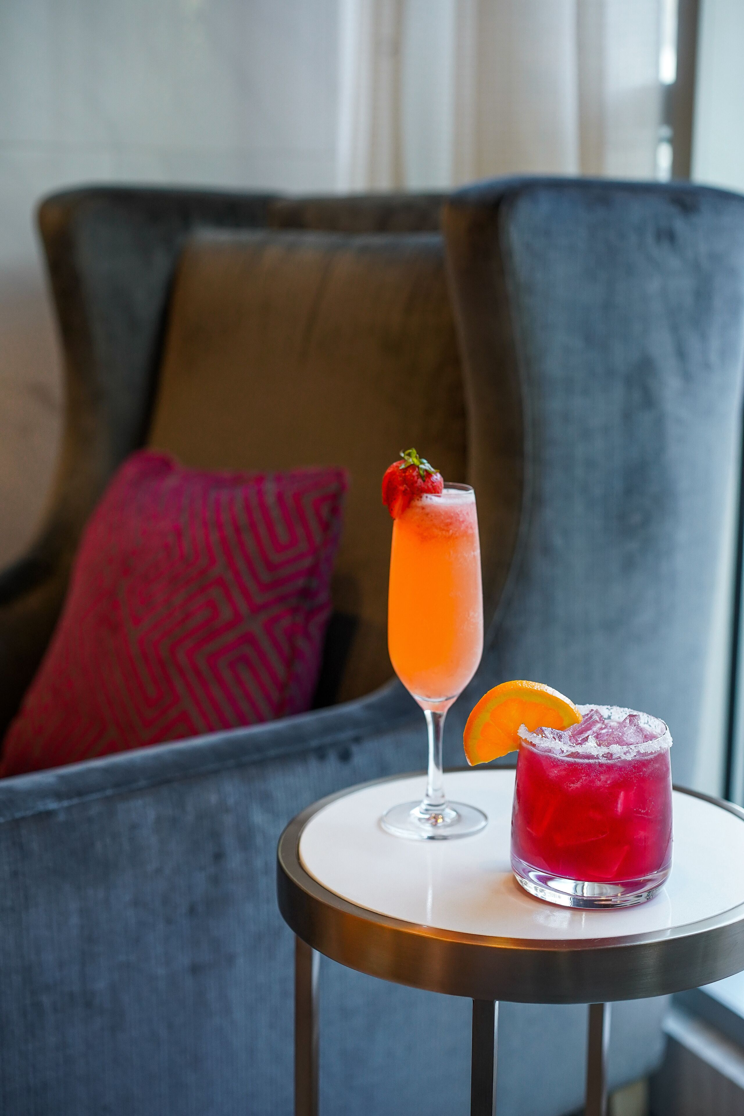A cocktail on a small round table with a sofa and a patterned pillow in the background.