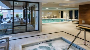 A modern indoor pool area with a hot tub, seating, and a glass-enclosed lounge area. - Hilton Garden Inn Seattle Bellevue Downtown, WA (Bellevue)