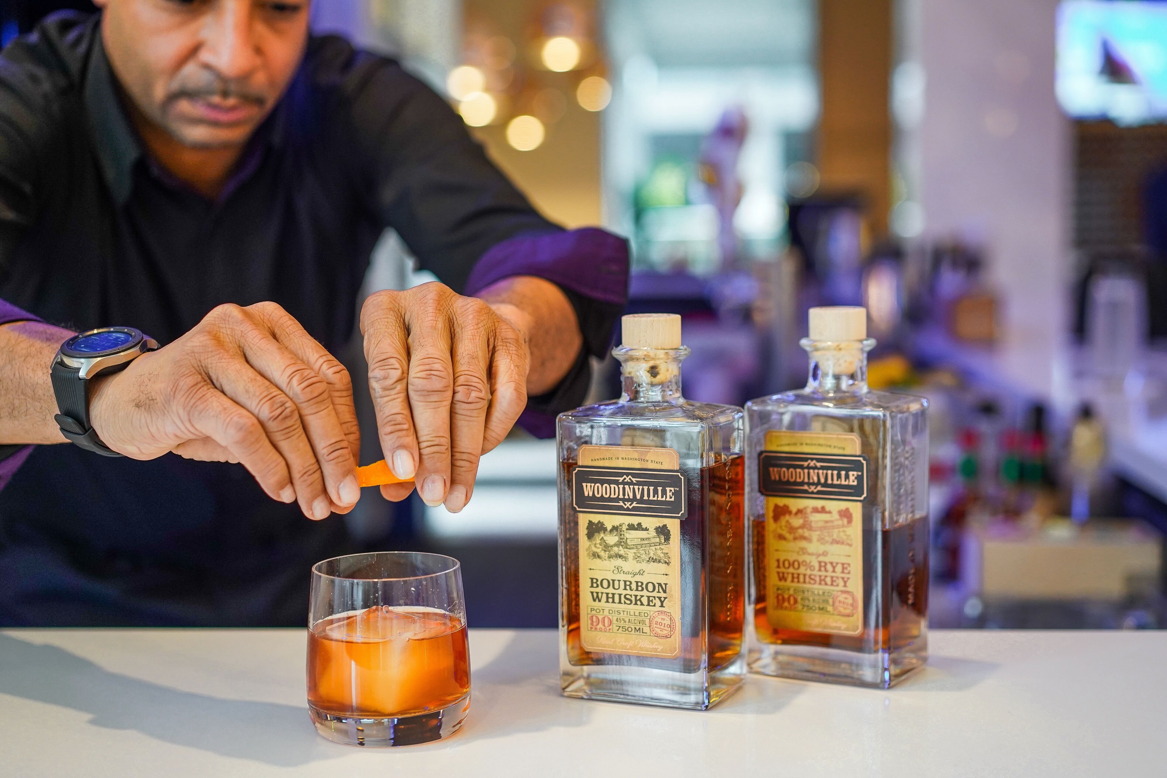 Una persona abocant una beguda d'una ampolla amb la inscripció 'Woodinville Bourbon Whiskey' a un got.
