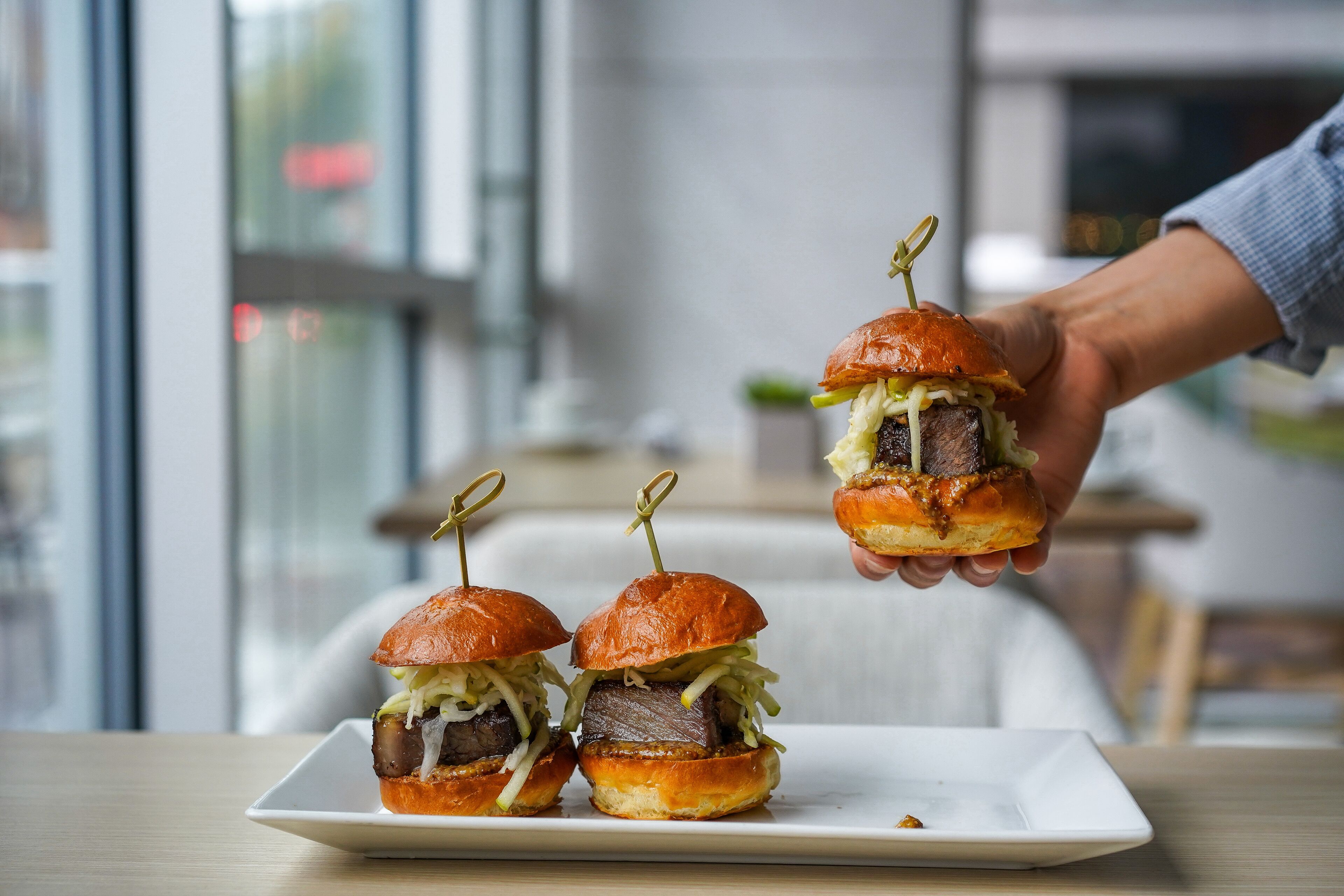 A plate with three mini burgers on a white rectangular plate.