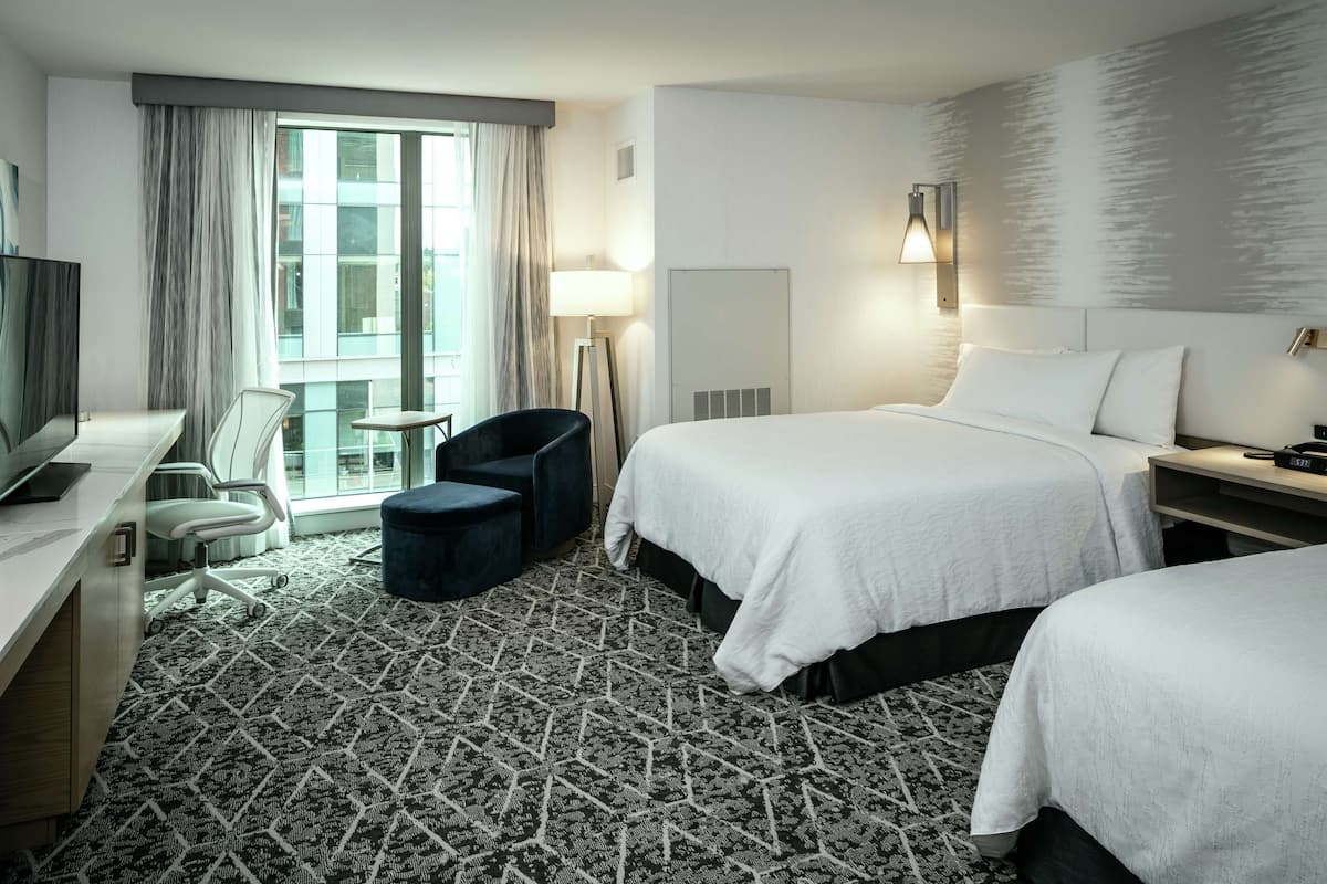 A hotel room with a large bed, a desk with a computer, a chair, a lamp, and a view of the city through the window.