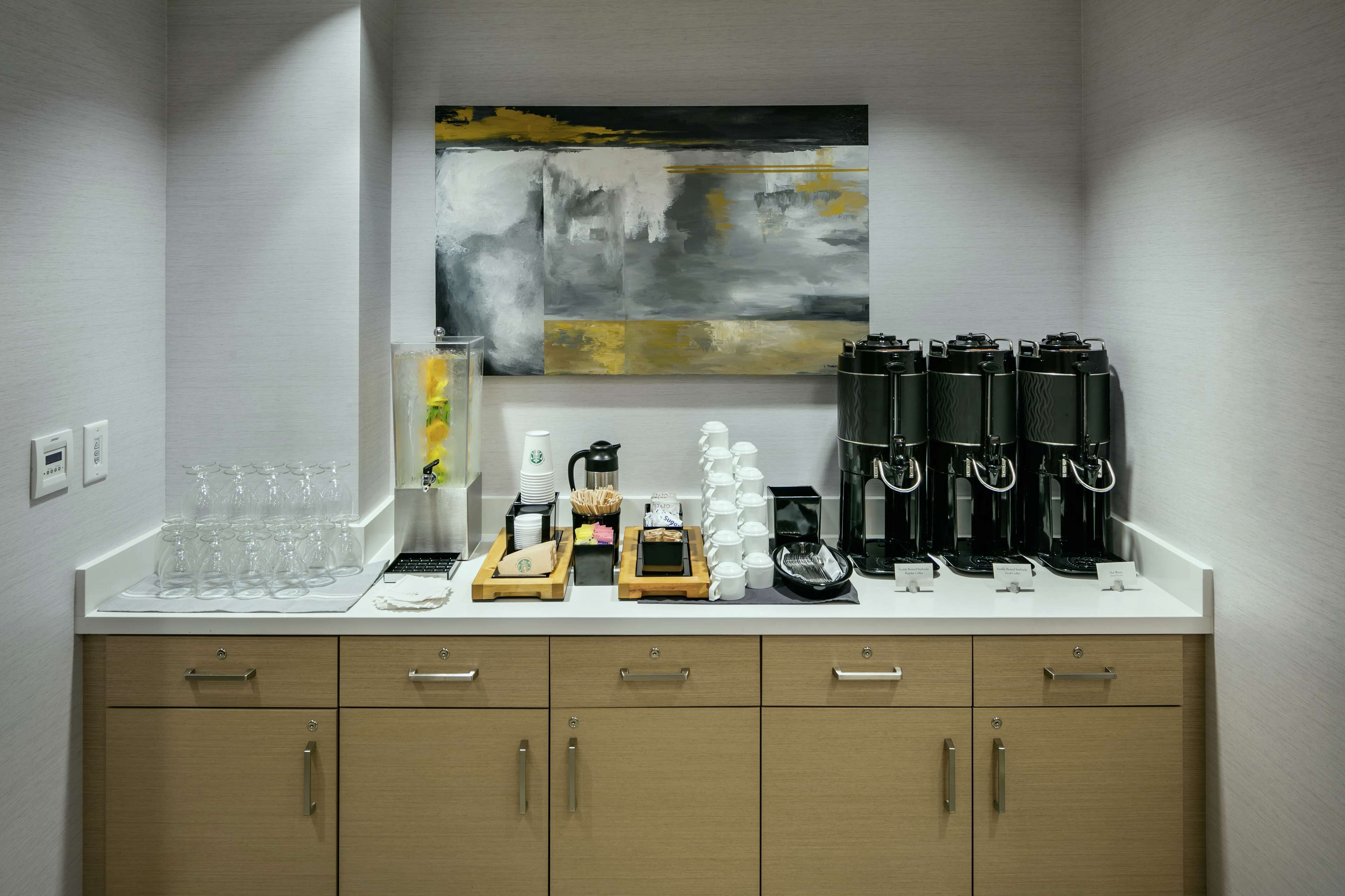 A breakfast bar with coffee makers, cups, and a coffee grinder.