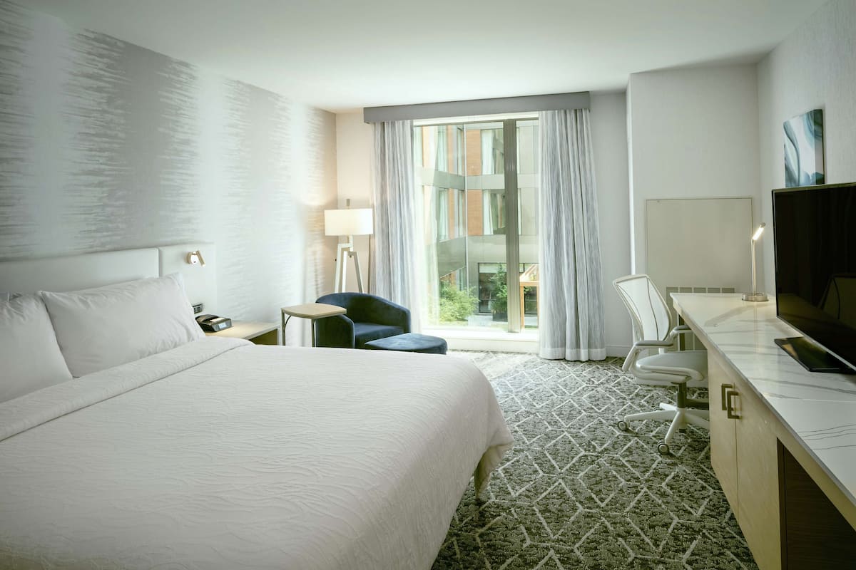 A hotel room with a large bed, a desk with a TV, a chair, and a window with curtains.