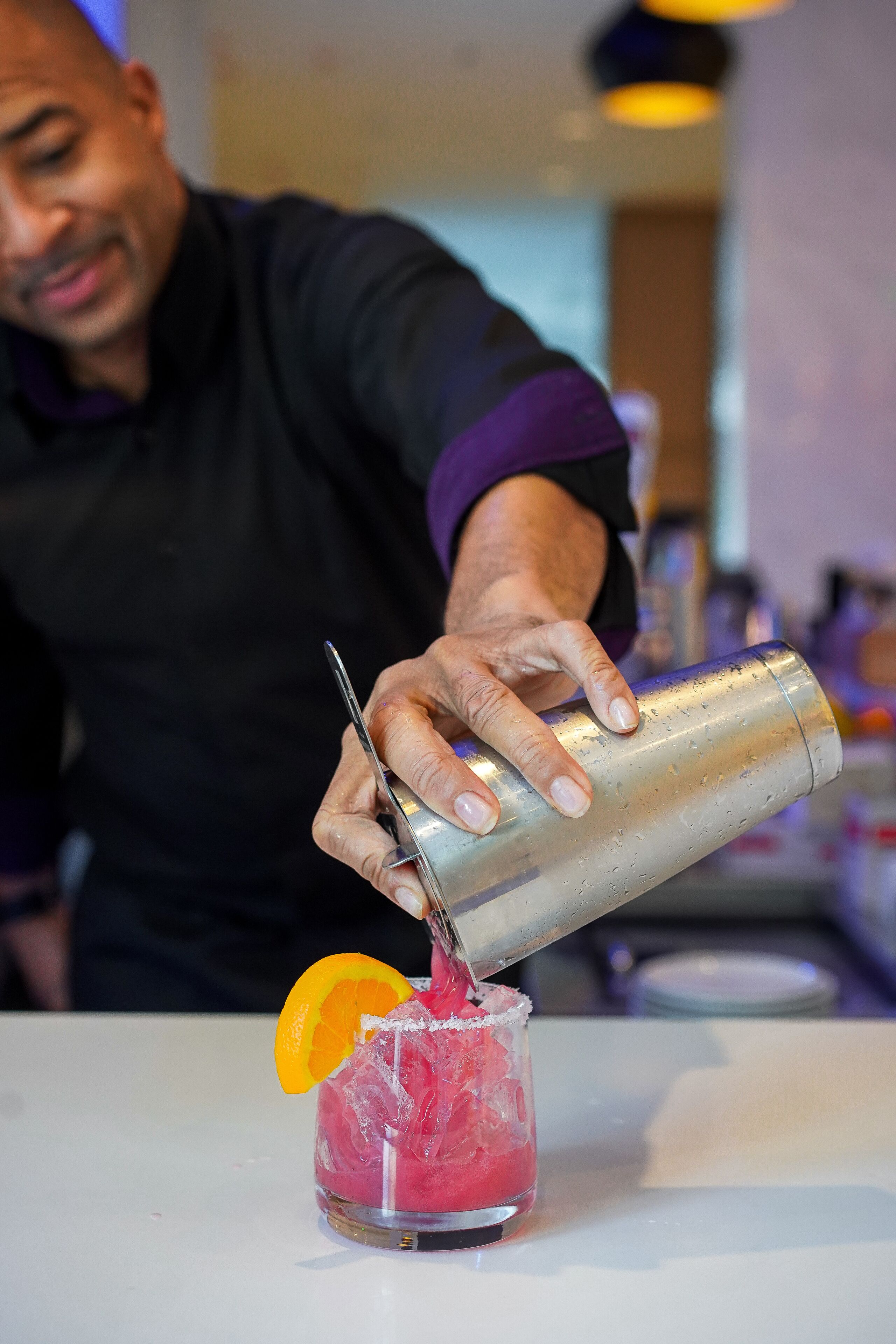 A bartender pouring a drink into a glass with an orange slice garnish.
