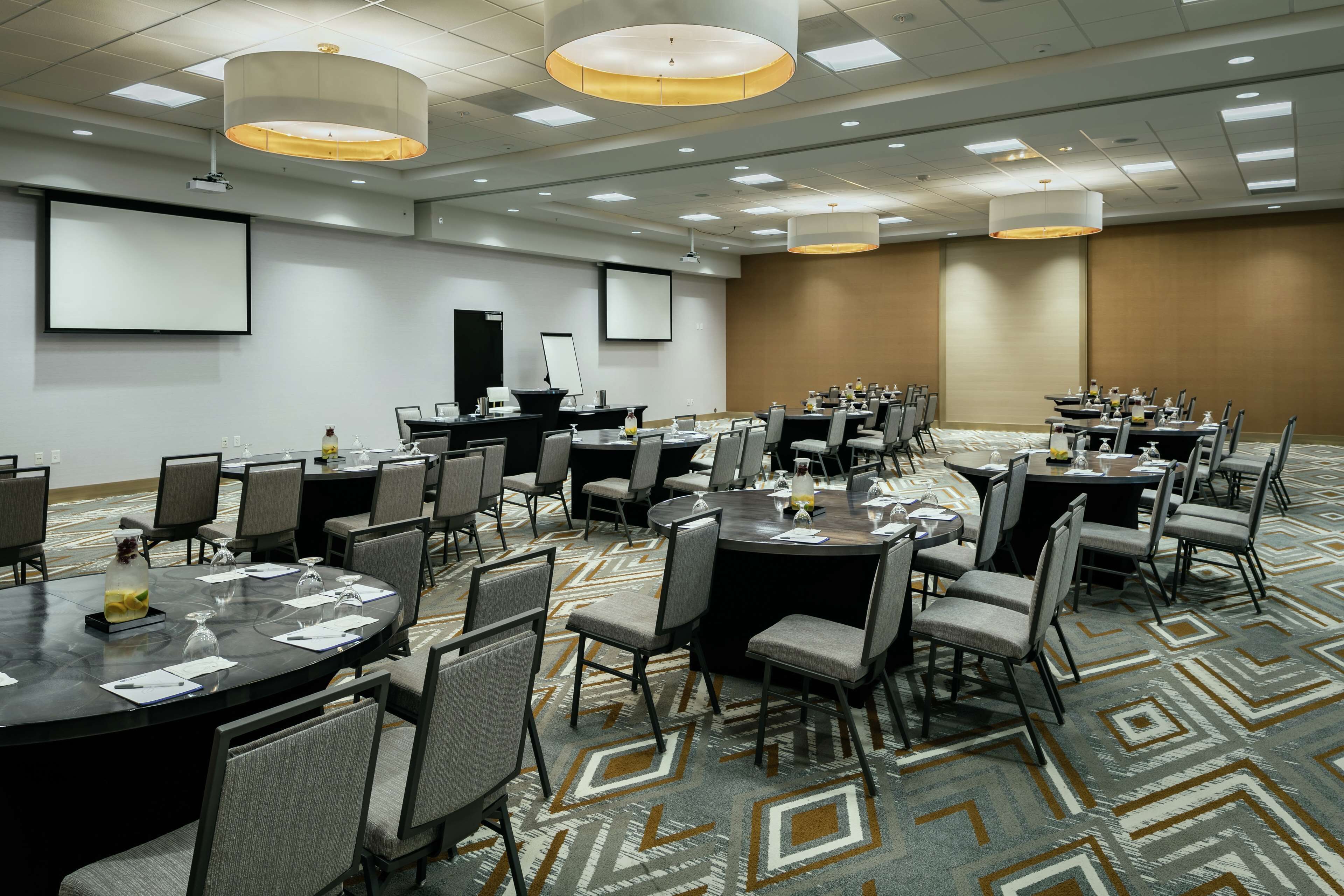 A conference room with multiple tables and chairs, equipped with projectors and screens.