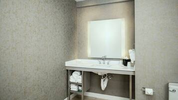 A bathroom with a white sink, mirror, and towel rack. There is a shelf under the sink holding folded towels.