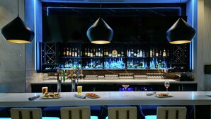 A bar area with a long counter, multiple hanging pendant lights, and a well-stocked bar with various bottles and glasses. - Hilton Garden Inn Seattle Bellevue Downtown, WA (Bellevue)