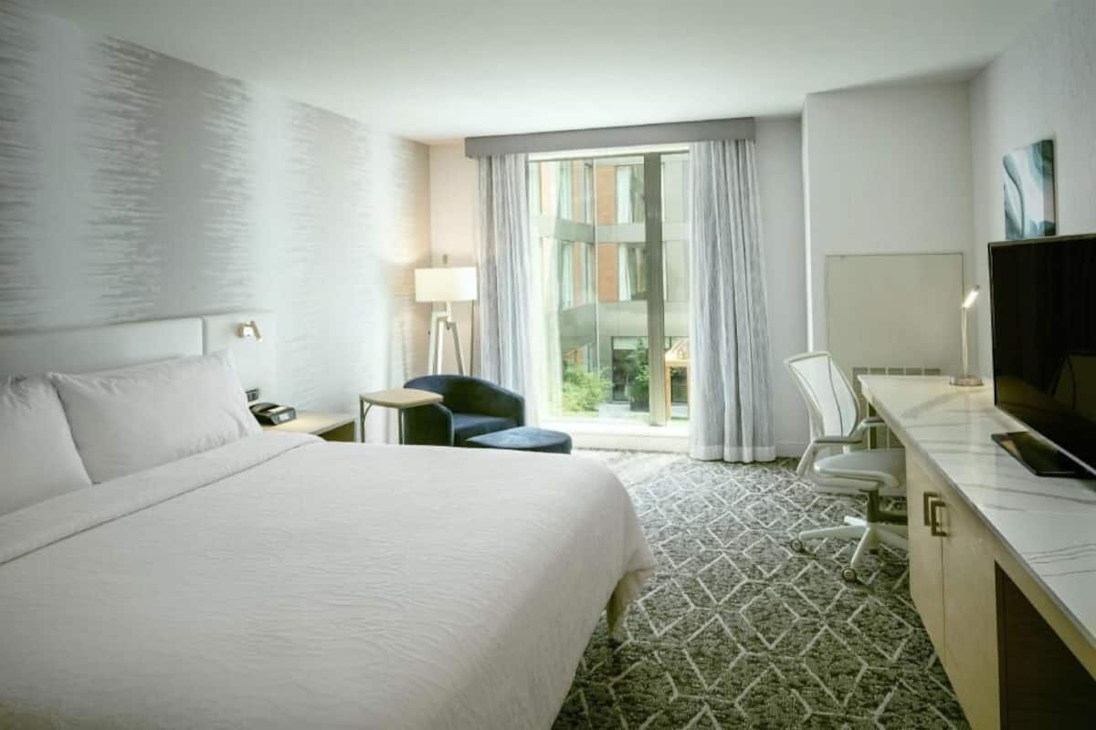 A hotel room with a large bed, a desk, a chair, a lamp, and a TV.