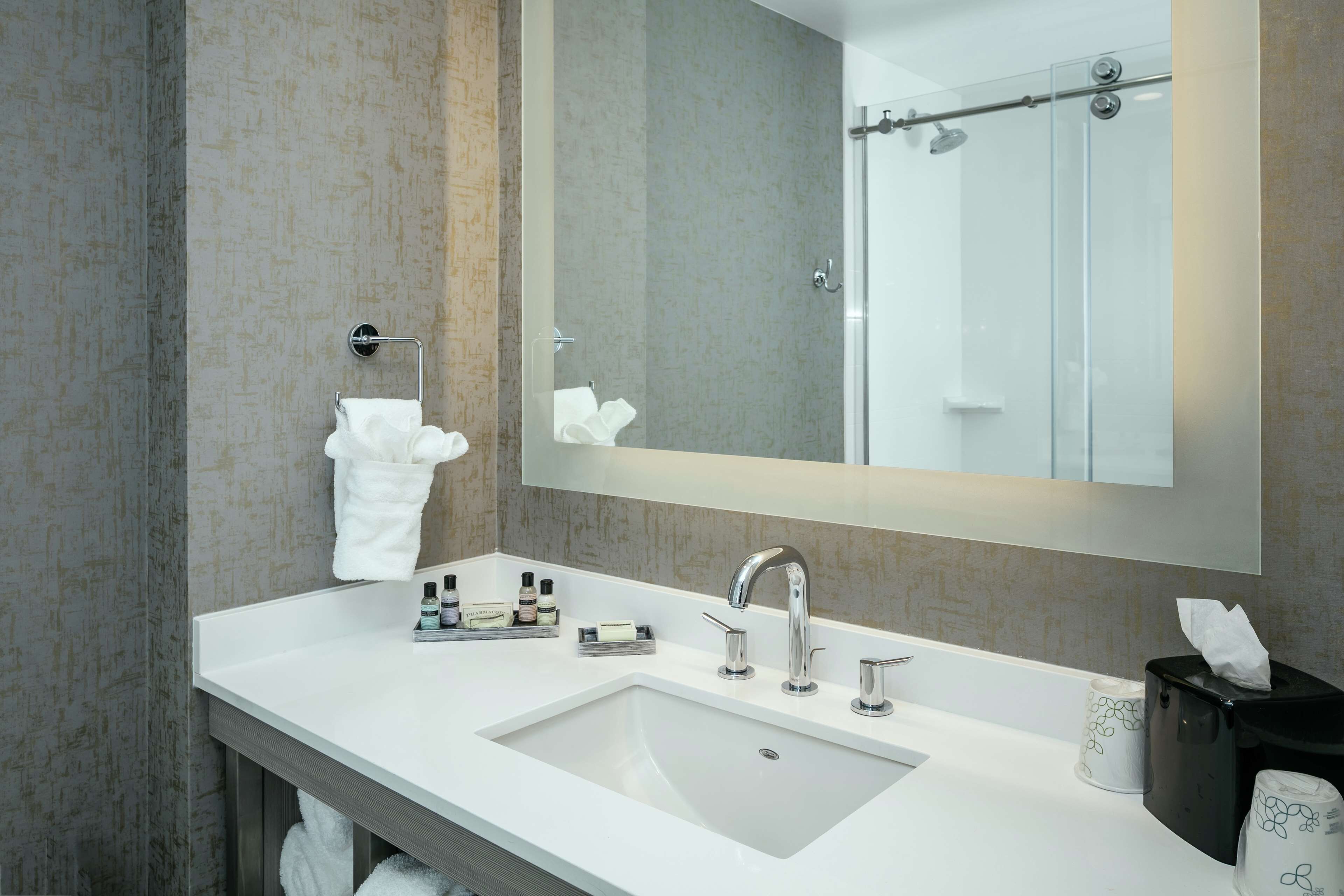 Ein modernes Badezimmer mit einem weißen Waschbecken, einem großen Spiegel und einer Duschkabine aus Glas.
