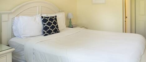 A neatly made bed with white bedding and a single black and white patterned pillow.