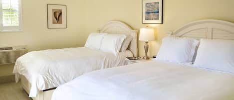 Une chambre d’hôtel avec deux lits, un ventilateur de plafond, une fenêtre avec des stores et deux tableaux encadrés accrochés au mur.