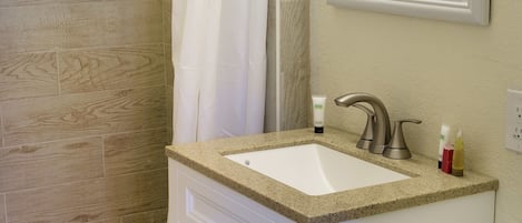 A bathroom with a shower, a sink with toiletries, and a toilet.