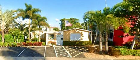 A small building with a flag, surrounded by palm trees and a parking lot.