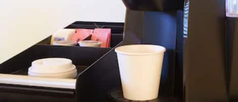 Una máquina de café con vasos desechables y tapas, una pequeña bandeja con una taza y una tapa, y una caja de pañuelos.