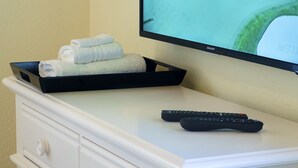 Un televisor que muestra un campo de golf, una bandeja con toallas dobladas y un control remoto sobre un tocador blanco.