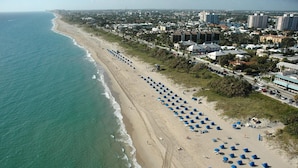 A coastal cityscape with a long beach lined with blue umbrellas and a clear view of the ocean. - Atlantic Hideaway (Delray Beach)