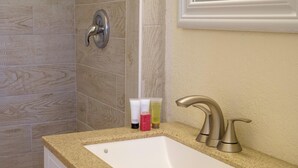 Un baño con encimera color beige, lavamanos blanco y zona de ducha con azulejos color beige.