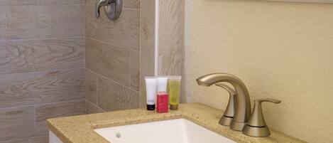 A bathroom with a beige countertop, a white sink, and a shower area with beige tiles.