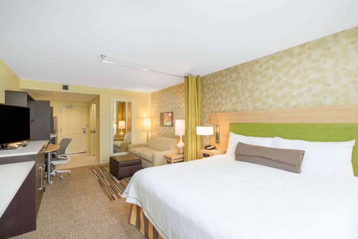 A hotel room with a bed, a desk, a chair, a television, and a mirror.