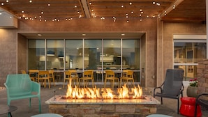 An outdoor seating area with a stone fire pit, yellow chairs, and a modern building in the background.