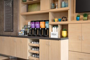 A hotel kitchenette with a coffee station, labeled mugs, and a sign for Hilton Honors.