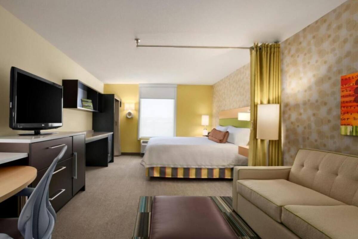 A hotel room with a bed, a sofa, a desk with a television, and a window.