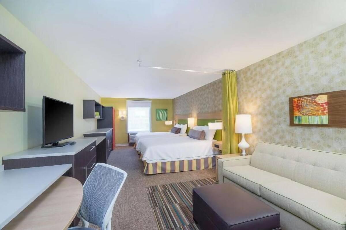 A hotel room with a bed, desk, chair, sofa, TV, and lamps.