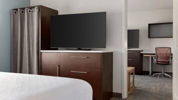 A hotel room with a bed, a TV on a wooden cabinet, a desk with a chair, and a shower area.
