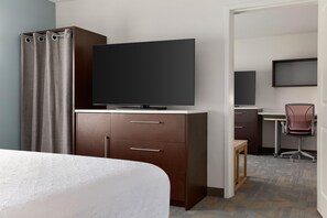 A hotel room with a bed, a TV on a wooden cabinet, a desk with a chair, and a shower area.