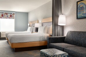 A hotel room with a bed, a sofa, a patterned ottoman, a lamp, and a painting on the wall.