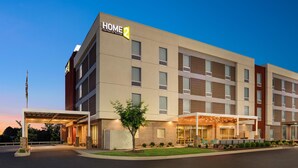 A modern hotel with a 'HOME 2' sign, a covered entrance, and outdoor seating.