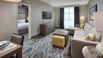 A hotel room with a bed, a sofa, a desk, a TV, and a window with curtains.