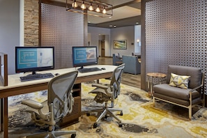 A hotel lobby with two computer workstations, a seating area with a chair and a small table, and a decorative wall with a geometric pattern. - Homewood Suites by Hilton Los Angeles Redondo Beach (Redondo Beach)