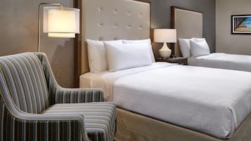 A hotel room with two beds, a chair, and a nightstand with a lamp.