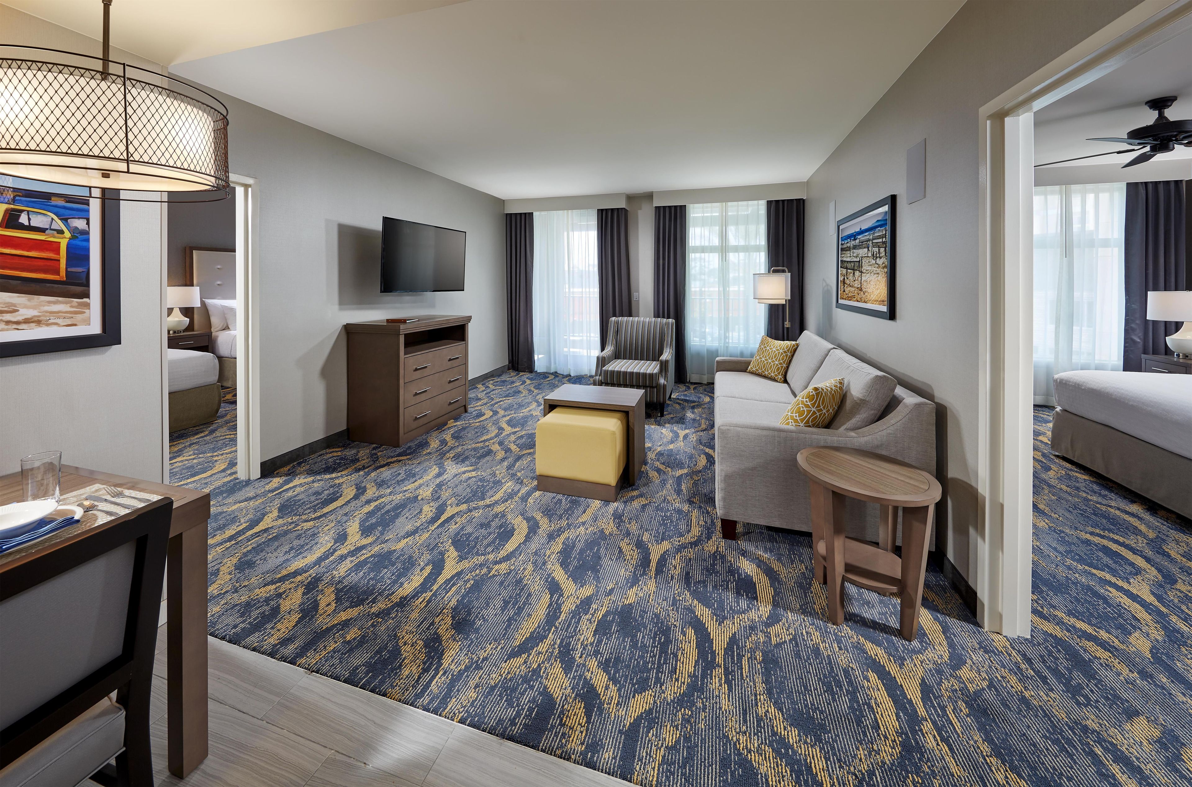 Habitación de hotel con cama, sofá, escritorio, televisor y alfombra estampada.