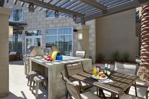 Un patio exterior con una parrilla, mesa de comedor, sillas y un pequeño espacio para sentarse.