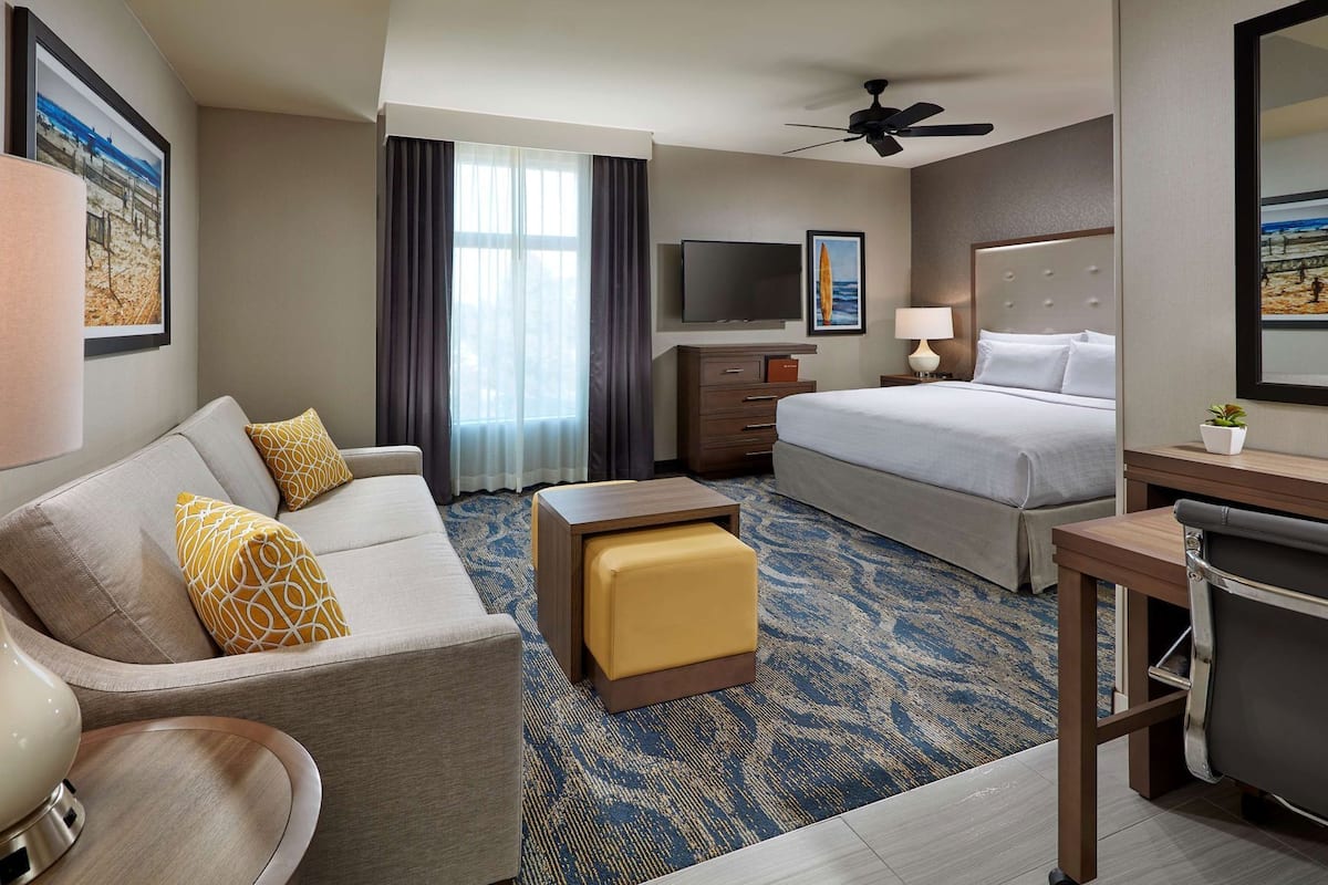 A hotel room with a bed, a sofa, a desk, a TV, and a ceiling fan.