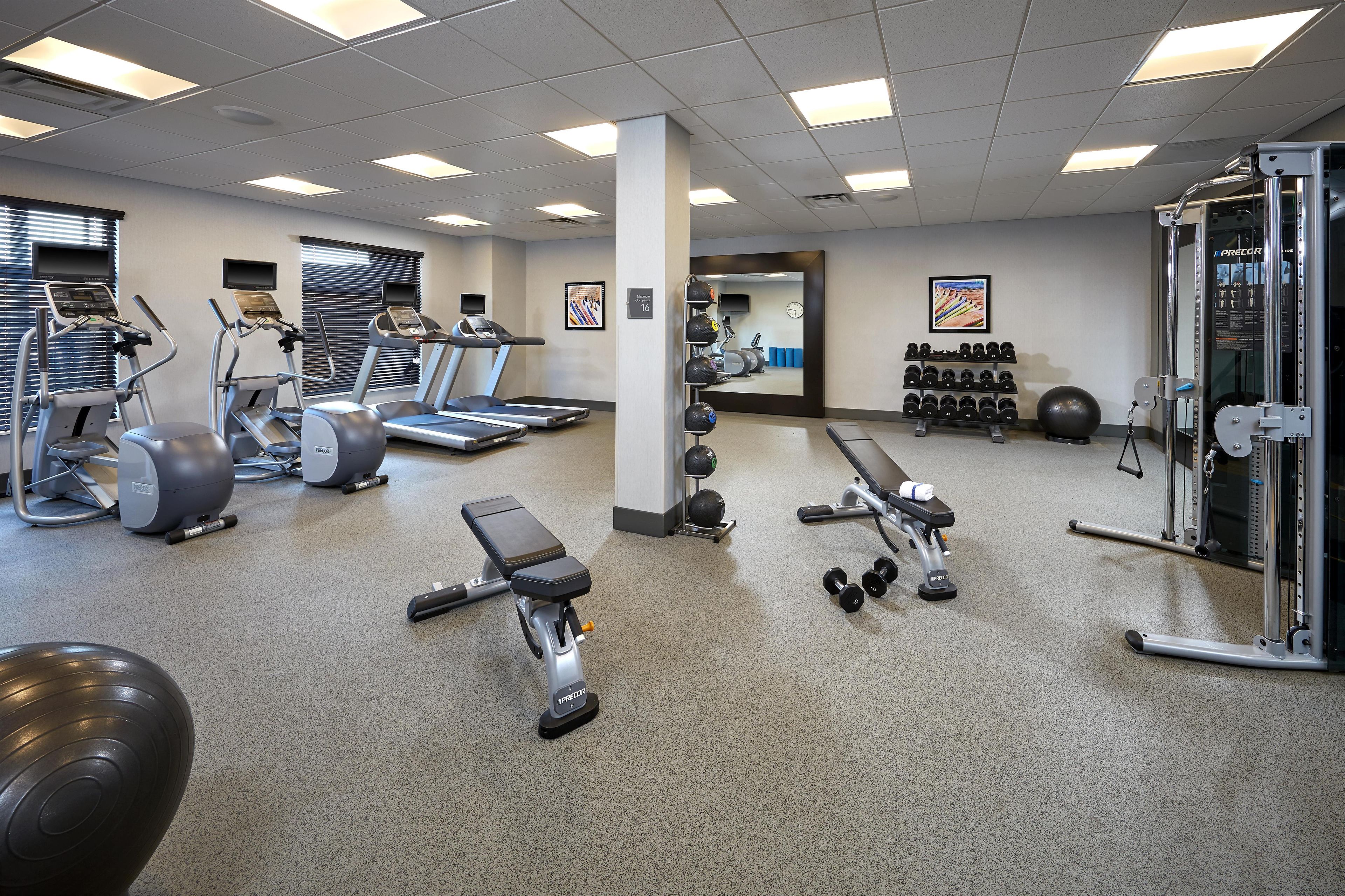 A gym with treadmills, elliptical machines, free weights, and a mirrored wall.