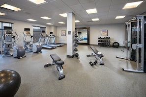 A gym with treadmills, elliptical machines, free weights, and a mirrored wall.
