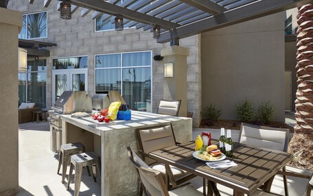 An outdoor patio with a grill, dining table, and chairs.