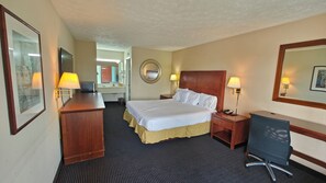 A hotel room with a bed, desk, chair, bedside lamps, a mirror, and a bathroom visible in the background. - Travelodge by Wyndham Richmond Kentucky (Richmond)
