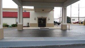 A covered parking area with a building entrance, a red awning, and a black vehicle parked inside. - Travelodge by Wyndham Richmond Kentucky (Richmond)