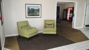 A hallway with two green armchairs, a framed landscape painting, and a red vending machine. - Travelodge by Wyndham Richmond Kentucky (Richmond)