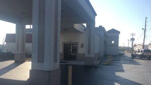 A building with a covered entrance, a door, and a parking area with vehicles. - Travelodge by Wyndham Richmond Kentucky (Richmond)