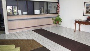 A reception area with a check-in counter, a potted plant, a desk with files, and a framed picture on the wall. - Travelodge by Wyndham Richmond Kentucky (Richmond)