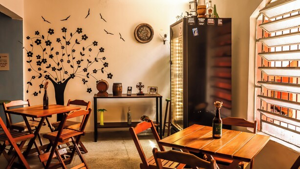 Un coin repas chaleureux, avec des meubles en bois, un mur décoratif orné d’un arbre et d’oiseaux, et un bar avec des bouteilles et une enseigne.