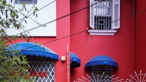 Un bâtiment rouge avec une fenêtre blanche, un auvent bleu et une porte agrémentée d’une fresque colorée.