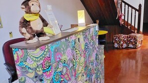 Un comptoir d’accueil orné d’un motif floral coloré, décoré d’un singe en peluche et agrémenté d’une petite table sur laquelle est posé un panneau lumineux.