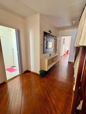 A hallway with wooden flooring, a sliding glass door, a small green basket, and a wall-mounted shelf with decorative items. - Red Monkey Hostel: Barra Funda (São Paulo)